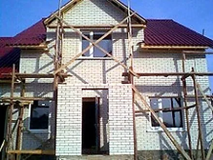 Вікна у новобудові з червоним дахом на етапі риштування